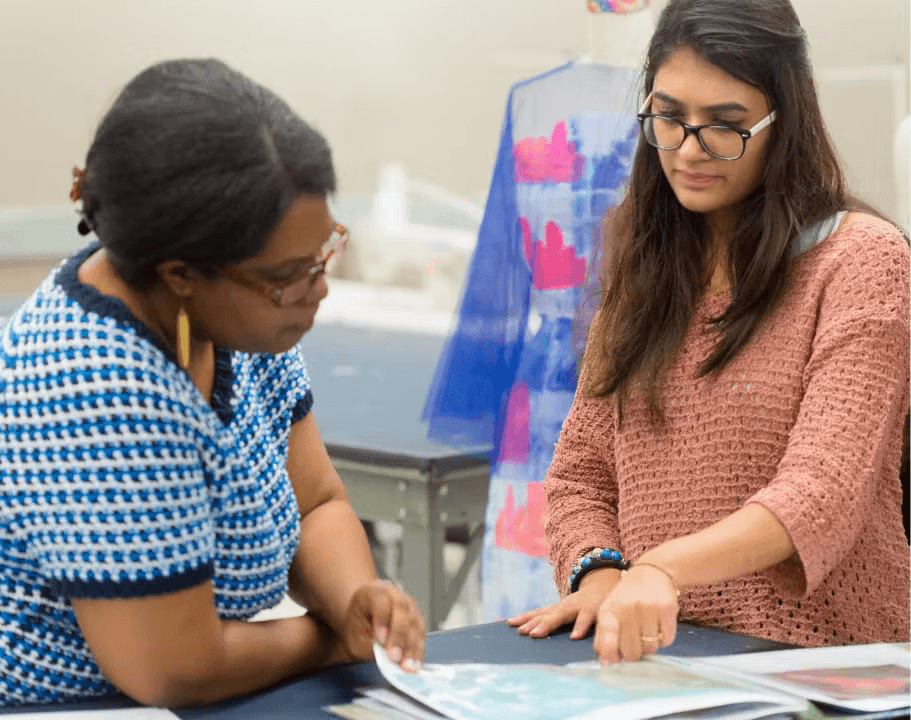 Two students looking through a fashion book as they design their own fashion pieces